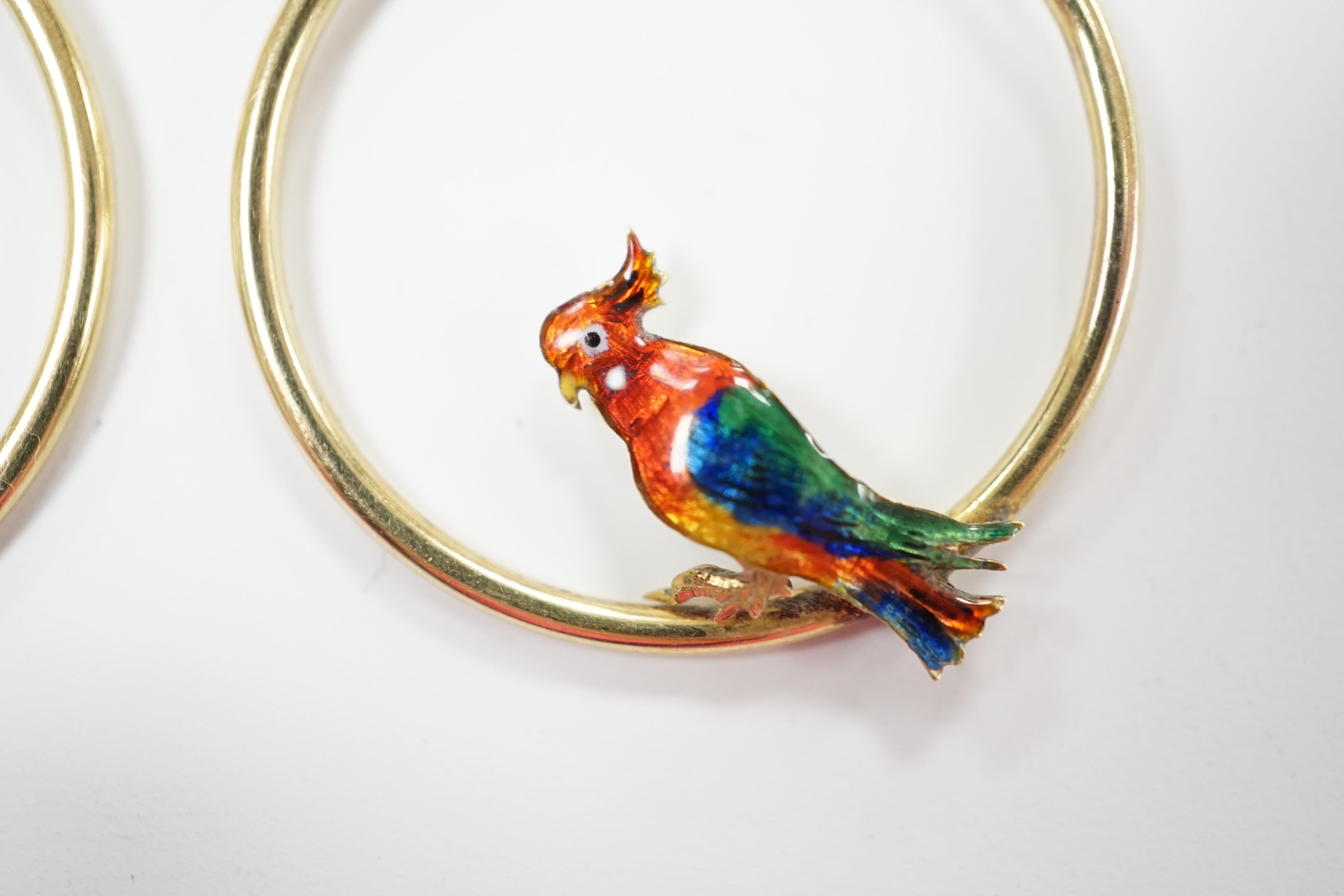 A pair of early 20th century 15ct loop ear clips, with a polychrome enamelled parrot perched upon each, diameter 30mm, gross weight 7.3 grams.